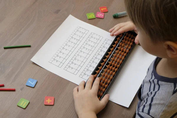 Kleine jongen die eenvoudige wiskunde oefeningen doet met abacus scores. Geestelijk rekenkundig. Zicht vanaf schouder — Stockfoto