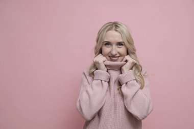 Pembe arka planda, yumuşak pembe, sıcak süveter giyen güzel sarışın kadın.