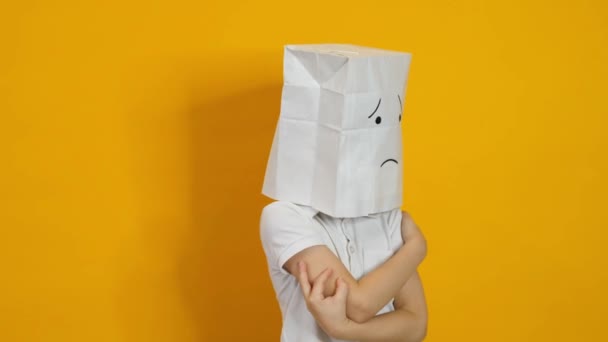 Μικρό αγόρι με μια τσάντα στο κεφάλι του - λυπημένο, απογοητευμένο πρόσωπο σε κίτρινο φόντο — Αρχείο Βίντεο