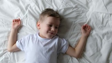 Cute little boy toddler wakes up, yawning and stretching on a bed in a bedroom. Close up