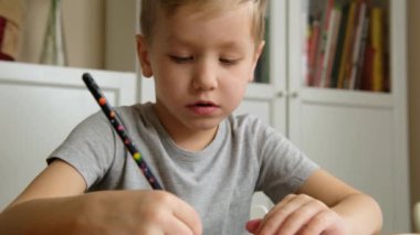 Cute preschool boy toddler, holding pencil, drawing or doing homework at the table