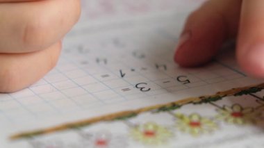 Anaokulu çocuğu, elinde kalem, yazı ya da masada matematik ödevi yapıyor. Eller yukarı.