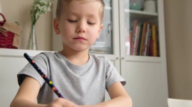 Anaokulu çocuğu, elinde kalem, çizim ya da masada ödev yapıyor.