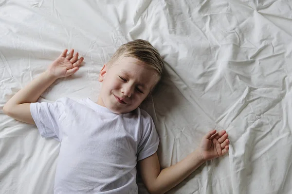 Roztomilý chlapeček batole spí ležet na bílé posteli v dopoledních hodinách, horní pohled — Stock fotografie
