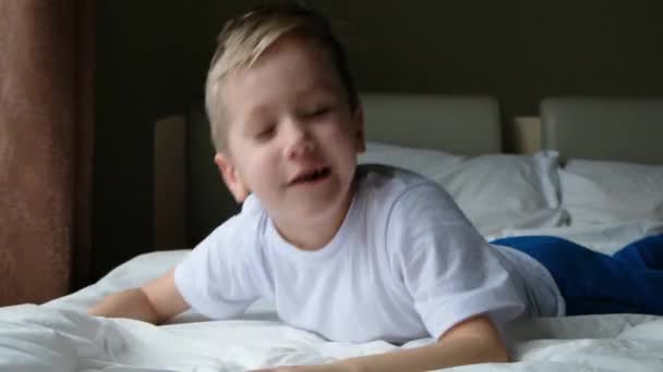 Niño divertido niño sonriendo y divirtiéndose. Se golpea la cabeza sobre una cama blanca y suave — Vídeos de Stock