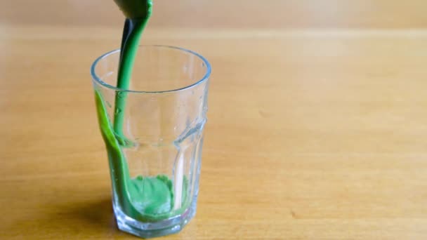 나무 탁자 위에 놓여 있는 유리잔에 건강에 좋은 녹색 스무디를 붓는 모습 — 비디오