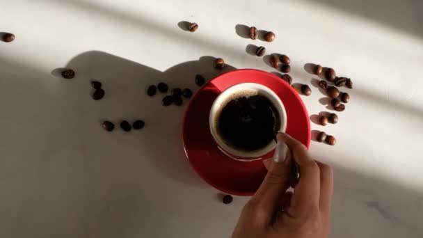 Womans mano revolviendo café en taza roja sobre mesa de mármol blanco con hermosa luz, vista superior — Vídeos de Stock