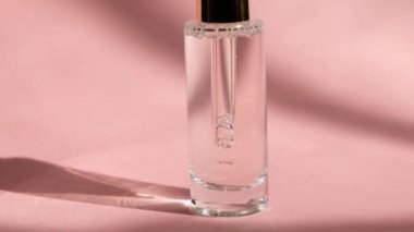 Pembe arka planda şeffaf cam şişede damlatan serum ve kadın eli, kapat. Cilt bakımı güzelliği, kozmetik özü