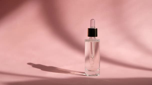 Suero gotero en frasco de vidrio transparente sobre fondo rosa y mano de mujer. Cuidado de la piel belleza, esencia cosmética — Vídeo de stock