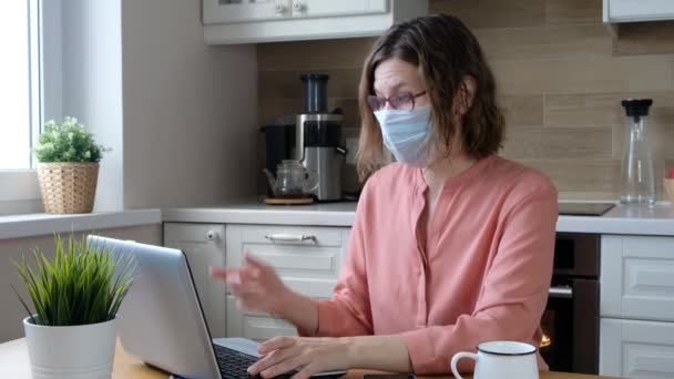 Een vrouw met een medisch masker die thuis werkt. Corona virus quarantaine, isolatieperiode covid - 19 — Stockvideo