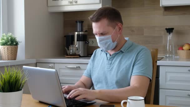 Een man met een medisch masker die thuis werkt. Corona virus quarantaine, isolatieperiode covid - 19 — Stockvideo