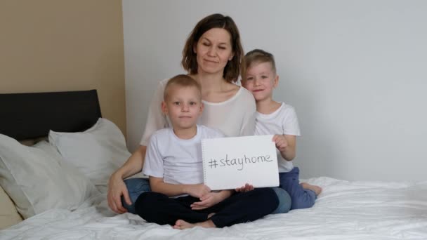 Rodzina siedząca w domu, trzymająca białą kartkę z tekstem "Zostań w domu". Kwarantanna koronawirusu — Wideo stockowe