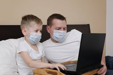 Korona virüsü karantinaya alınırken koruyucu maskeli ve çocuklu baba yatakta yatıyor. Uzaktan eğitim, evde kal.