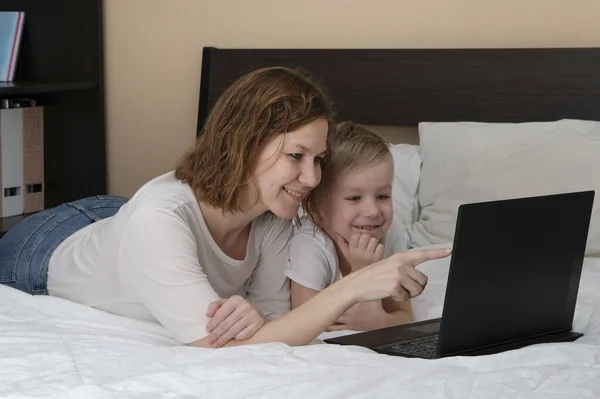带着孩子和手提电脑的妇女躺在床上，正在对日冕病毒进行检疫。远程教育，待在家里 — 图库照片