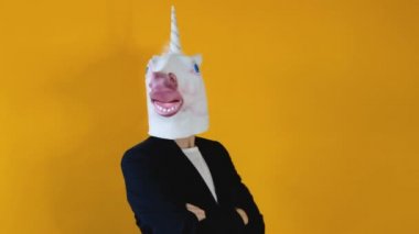 Tuhaf, komik bir video. Takım elbiseli, tek boynuzlu at kafalı, sarı arka planda duran bir iş kadını.