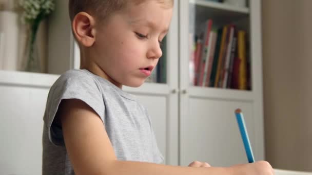 Óvodás fiú csecsemő, kezében ceruza, rajz vagy csinál házi feladatot az asztalnál — Stock videók