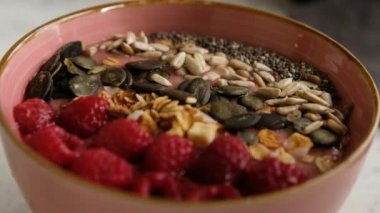 Birisi Granola ile ahududu Smoothie Bowl yiyor, tohumlar, kaşıkla chia, yakın çekim. Vejetaryen kahvaltısı