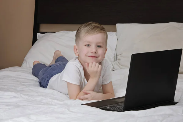 Niño lindo y portátil tumbado en la cama mientras que la cuarentena del virus corona. Educación a distancia, quedarse en casa — Foto de Stock