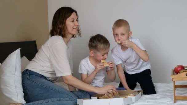 Familienmutter mit Kindern isst Pizza auf dem Bett und lächelt — Stockvideo