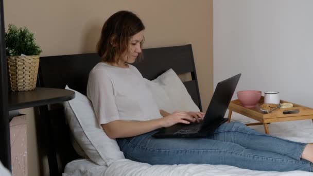 Frau, die zu Hause arbeitet, sitzt mit Laptop im Bett — Stockvideo