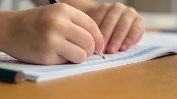 Niño en edad preescolar, sosteniendo lápiz, escribiendo o haciendo deberes en la mesa. Las manos de cerca — Vídeo de stock