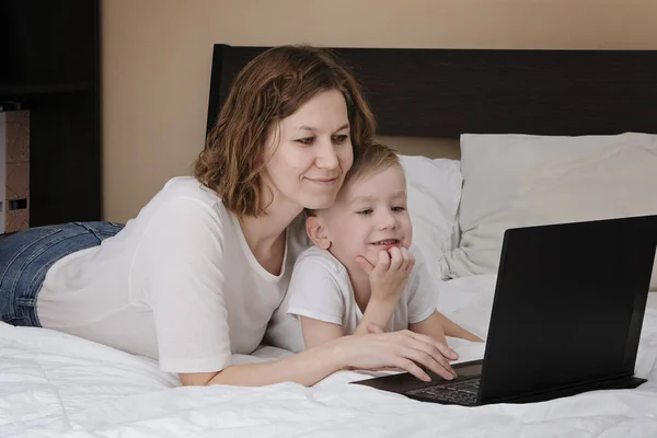 息子を持つ女性は、コンピュータでコロナウイルスの隔離中にベッドの上に横たわっています.遠隔教育家にいて — ストック写真