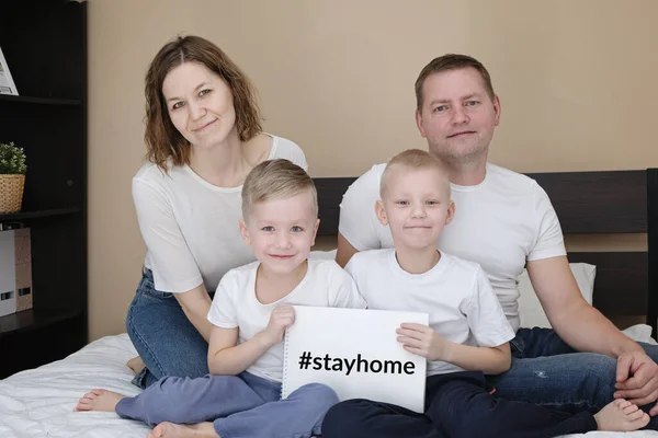 自宅のベッドに座っている子供たちと家族は、テキストSTAY HOMEと白い紙を保持します。コロナウイルスの隔離 — ストック写真