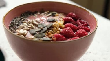 Birisi Granola ile ahududu Smoothie Bowl yiyor, tohumlar, kaşıkla chia, yakın çekim. Vejetaryen kahvaltısı