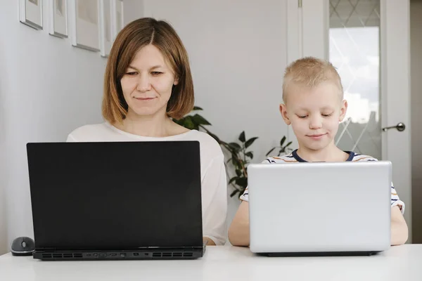 Una mujer joven y su pequeño hijo se sientan en una casa durante la cuarentena y estudian en la escuela de Internet usando una computadora. Distancia social — Foto de Stock