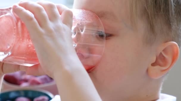 Divertido niño bebiendo jugo rojo fresco y mirando a la cámara con la cara feliz y la boca manchada. De cerca. — Vídeos de Stock