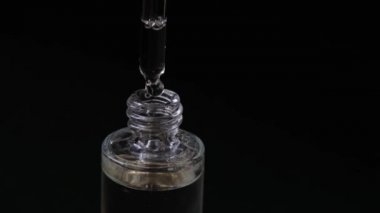 Kadınlar ellerinde cam bir şişe iquid, kolajen serumları tutarlar. Arka planda bulanık damlalar vardır. Kapatın. Siyah arkaplan