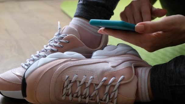 身穿运动服和运动鞋的妇女手持智能手机滚动体育网络应用程序，关门 — 图库视频影像
