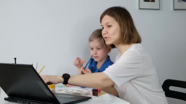 Маленький мальчик учиться рисовать онлайн с матерью через Интернет глядя на ноутбук, дистанционное образование , — стоковое видео
