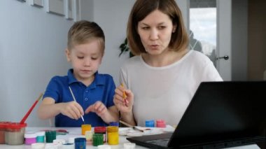 Küçük çocuk internetten annesiyle çizim yapıyor. Bilgisayara bakıyor, uzaktan eğitim görüyor.,