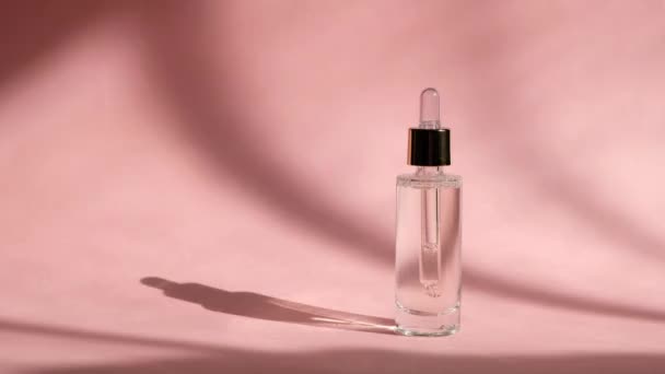 Suero gotero en frasco de vidrio transparente sobre fondo rosa y mano de mujer. Cuidado de la piel belleza, esencia cosmética — Vídeo de stock