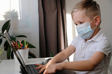 Uzaktan öğrenme çevrimiçi eğitim. Beyaz çocuk evde dizüstü bilgisayarla ödev yaparken epidemi korona virüsünü karantinaya almış.