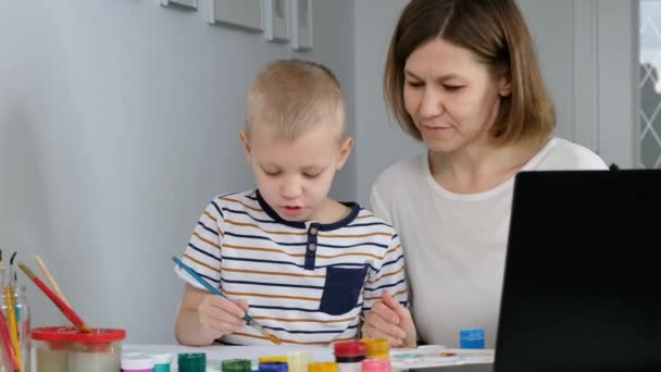 Маленький мальчик учиться рисовать онлайн с матерью через Интернет глядя на ноутбук, дистанционное образование , — стоковое видео
