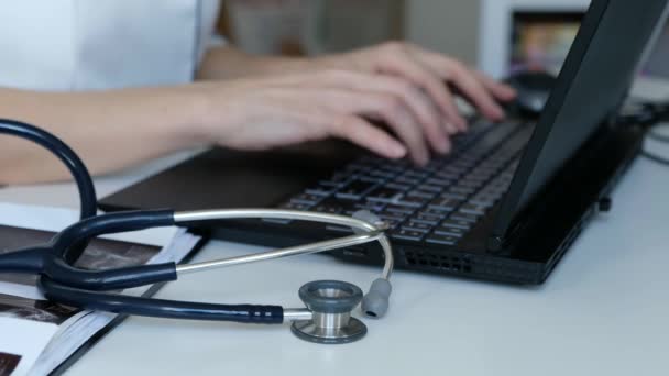 医生在电脑上工作键盘关闭桌子上的听诊器 — 图库视频影像