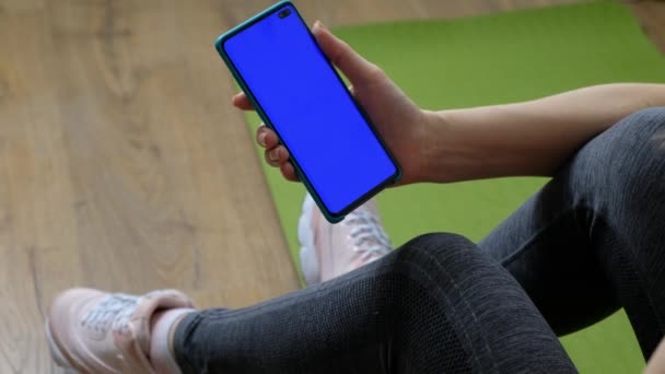 Mujer en ropa deportiva y zapatillas de deporte con teléfono inteligente con pantalla azul lugar para la aplicación web de deporte — Vídeo de stock