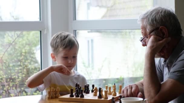 Mały chłopiec grać w szachy z dziadkiem, senior positive man — Wideo stockowe