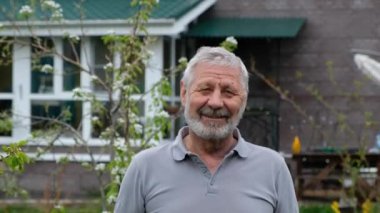 Kibar yüzlü yaşlı Senoir, dışarıda, evinin önünde kameraya bakıyor.