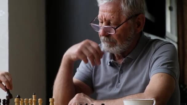 Niño pequeño jugar ajedrez con su abuelo, hombre positivo senior — Vídeo de stock