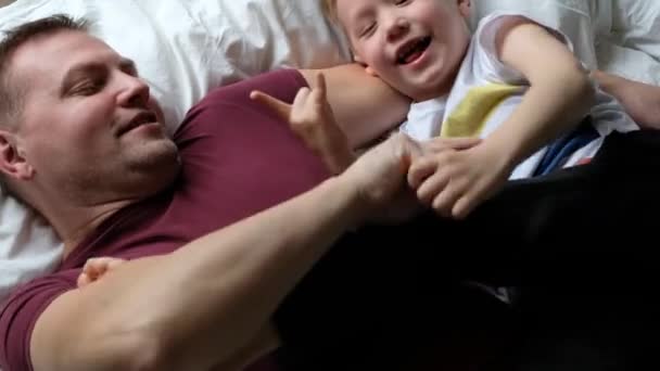 Glücklicher Vater, der sich mit seinem Sohn auf einem Bett amüsiert und lacht. Blick von oben — Stockvideo