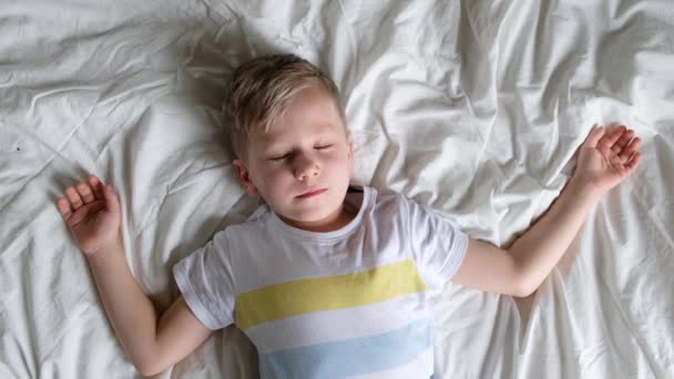 ベッドの上に寝そべっている小さな子供の男の子、ストレッチとあくび、目を覚ます概念 — ストック動画