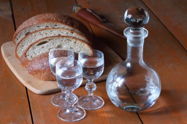 Sürahi ve üç bardak votka dilim ekmek yanında ahşap bir masa üzerinde duran.