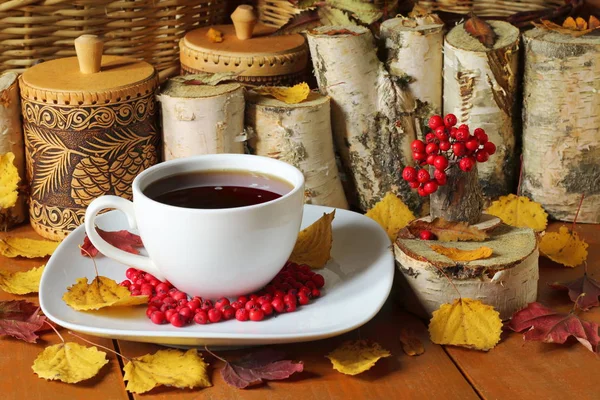 Auf dem Holztisch liegen ein Becher Tee, Beeren von Eberesche, Herbstblätter und Haushaltsgegenstände.. — Stockfoto