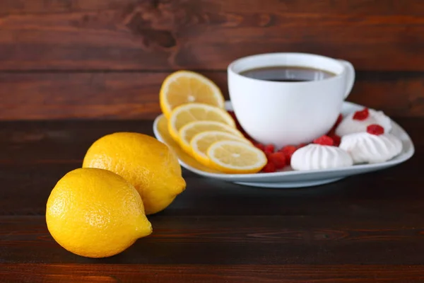 Lemon, black tea and sweets are on a dark wooden background.