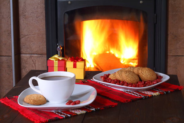 A mug of tea, plate of biscuits and gift boxes are on the table in front of the fireplace.