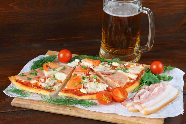 Pizza z mięsa wędzonego i kubek piwa są na ciemnym tle drewnianych. — Zdjęcie stockowe