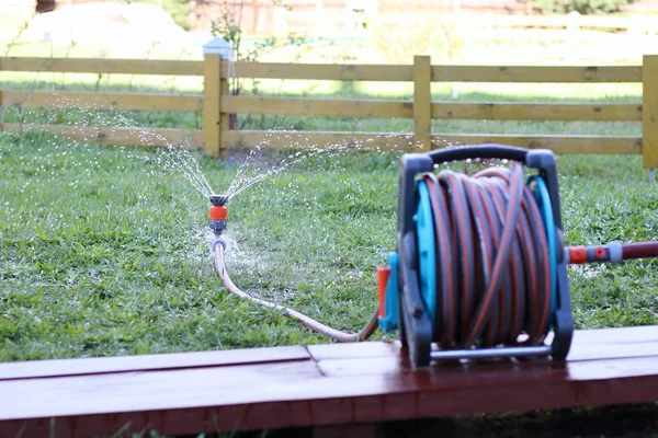 Sprinkler and reel with hose are in the garden. — Stock Photo, Image